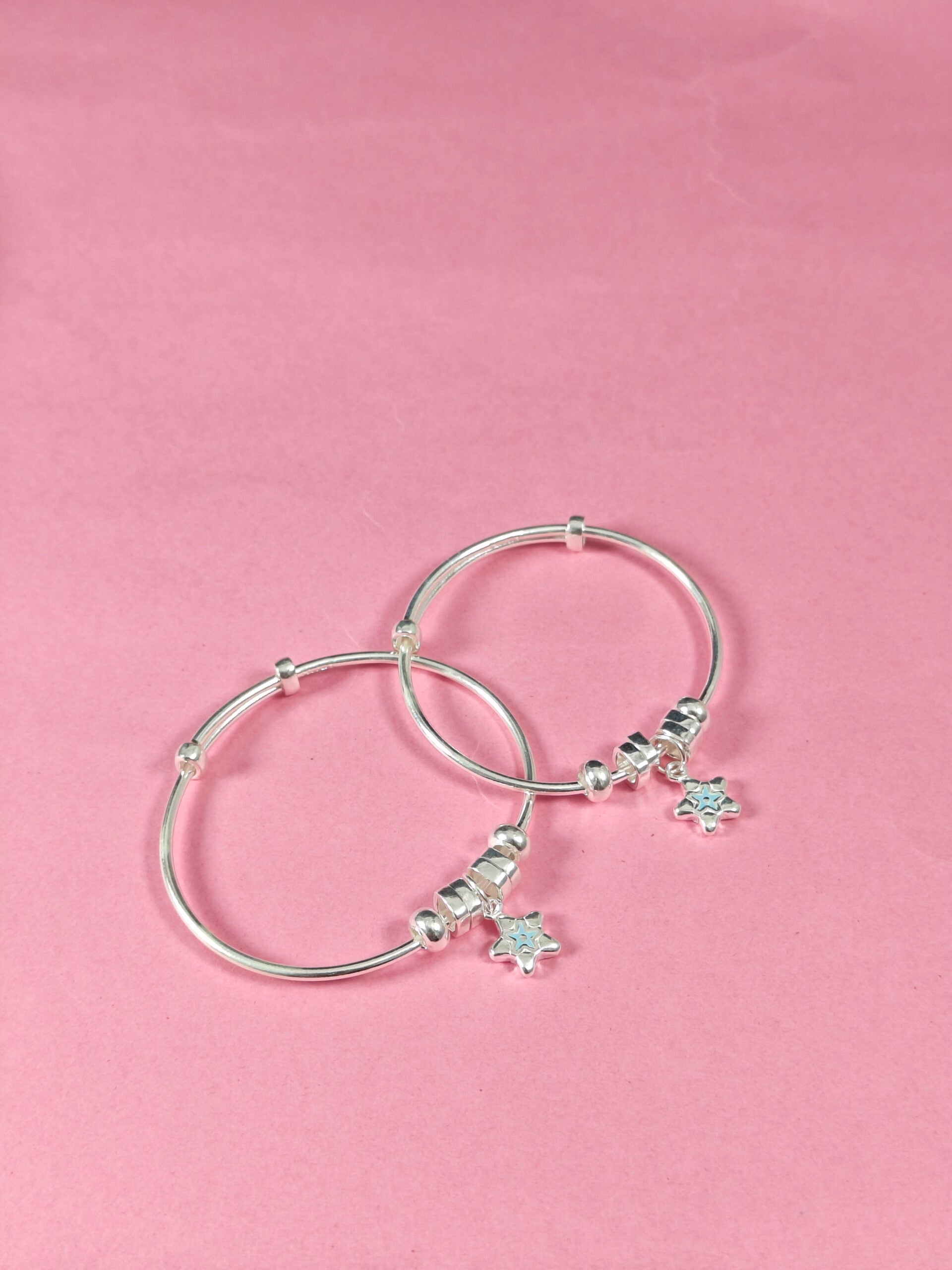 Two silver bangles with turtle charms on a pink background